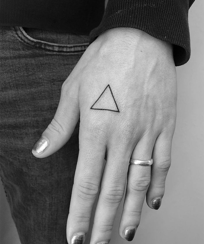 Triangle small tattoo on a person's hand with silver nails.