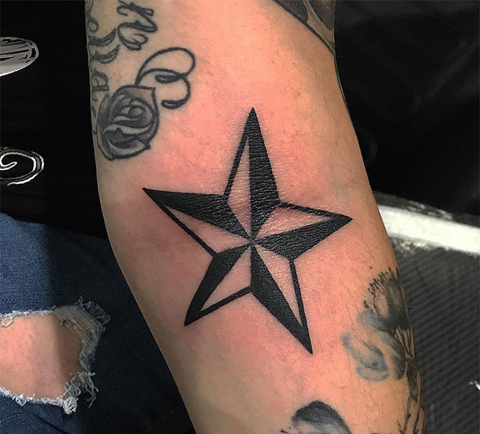 Black star tattoo on forearm surrounded by other small tattoos, showcasing unique small tattoo ideas.