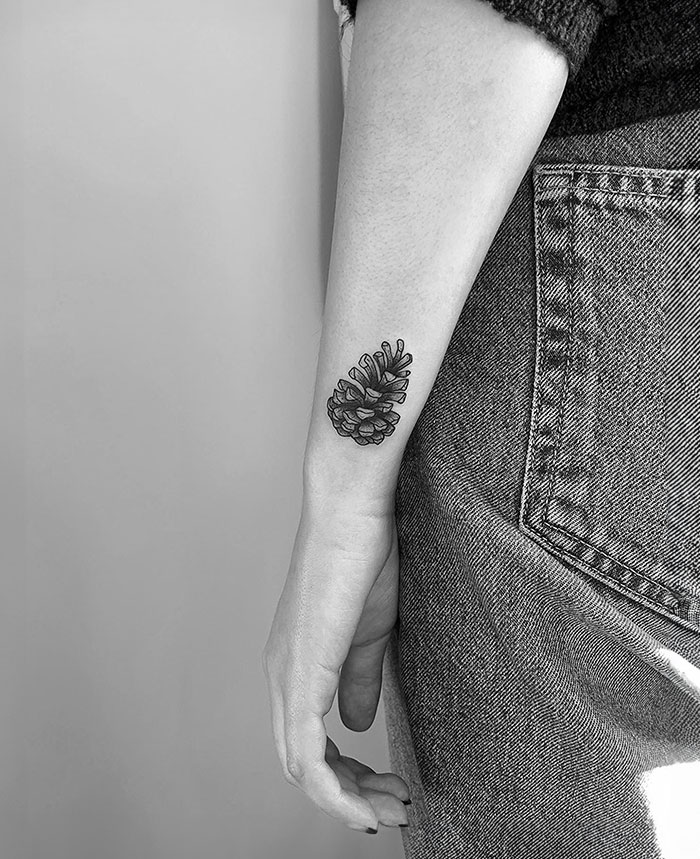 Small tattoo of a pine cone on forearm, simple and detailed, paired with casual jeans.