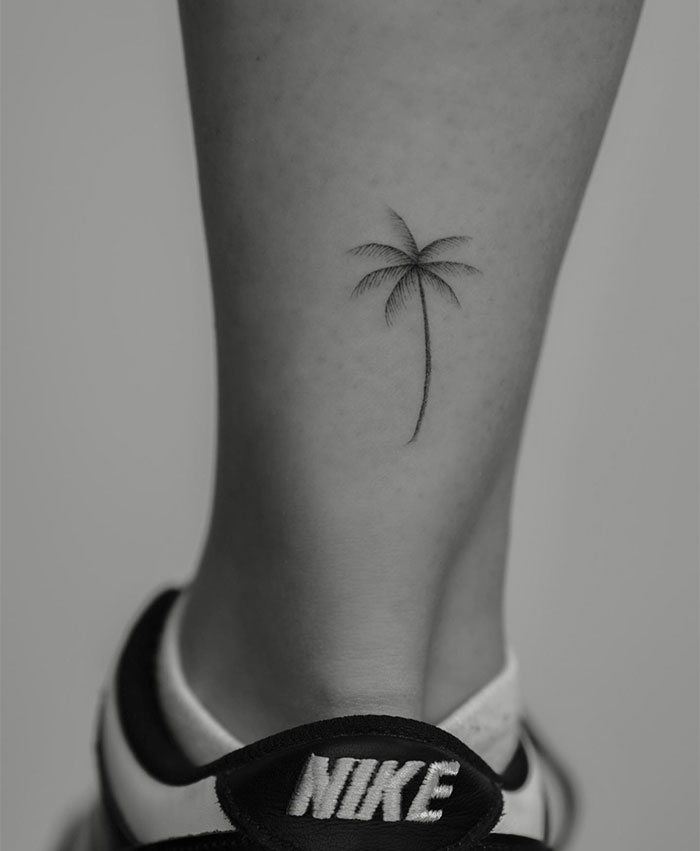 Small tattoo of a minimalist palm tree on a person's ankle above a Nike sneaker.