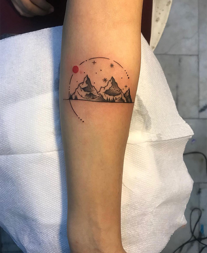 Mountain landscape small tattoo with stars and red sun on forearm, showcasing powerful design ideas.