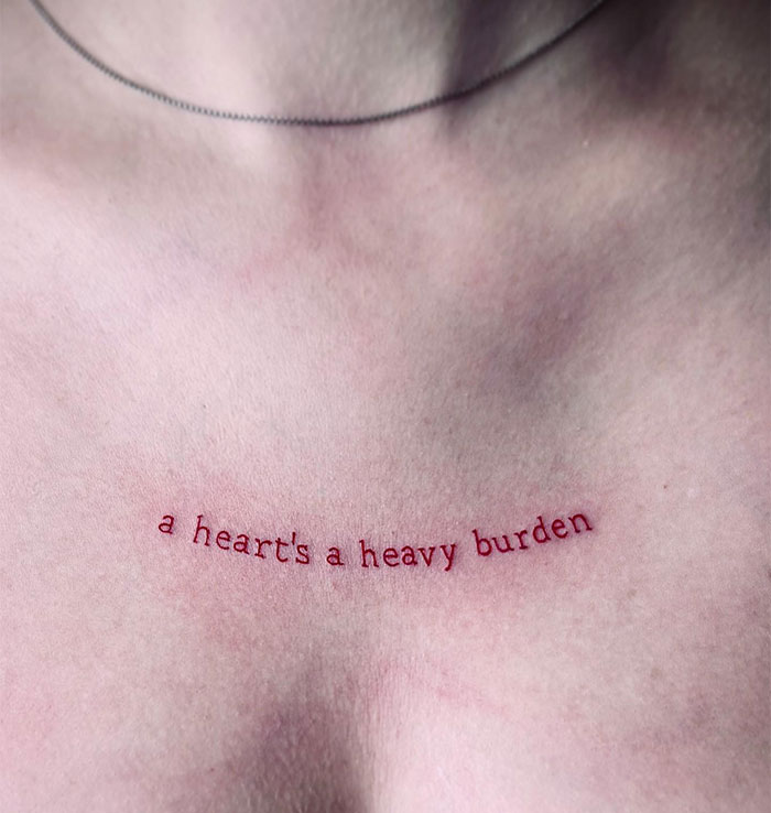 Minimalist small tattoo reading "a heart's a heavy burden" on skin.