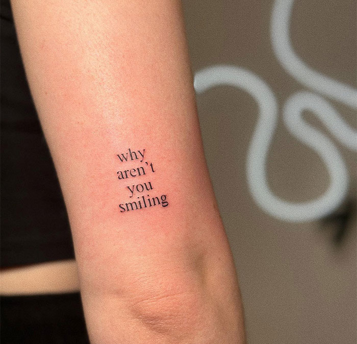 Minimalist small tattoo on arm with the phrase "why aren't you smiling," showcasing a compact design.