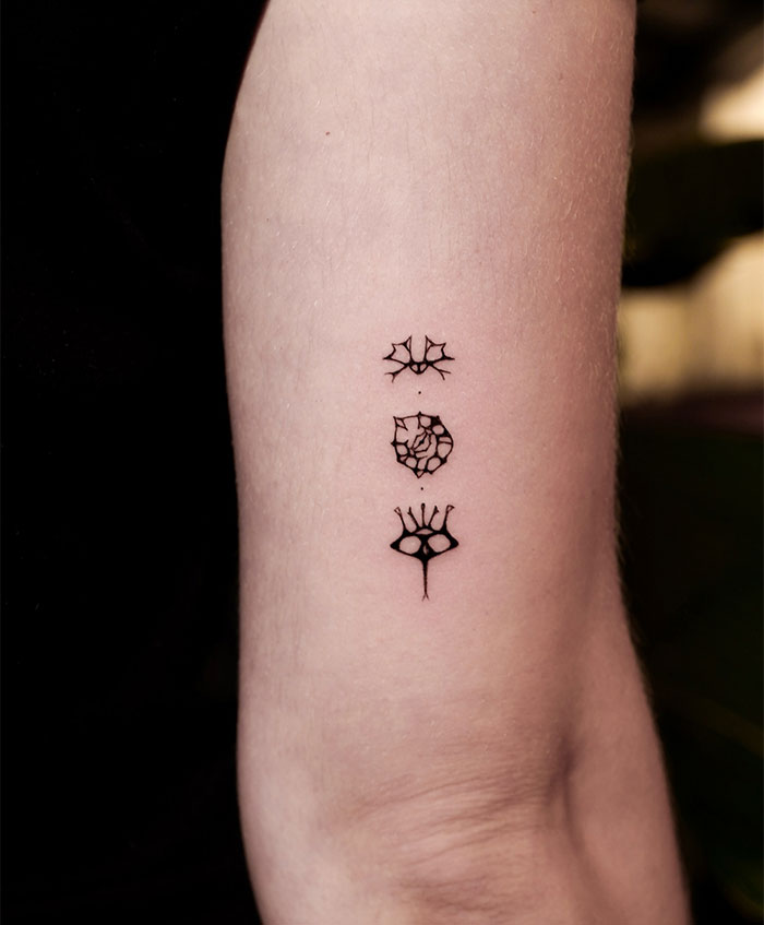 Minimalist small tattoo designs on an arm, showcasing intricate geometric patterns.