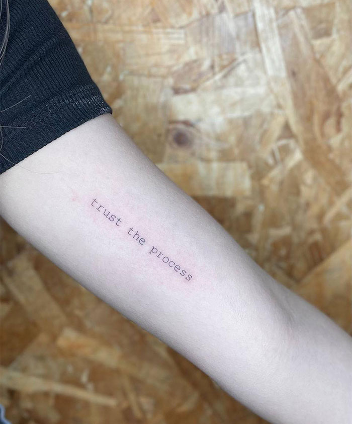 Small tattoo on forearm with text "trust the process" in minimalist style.