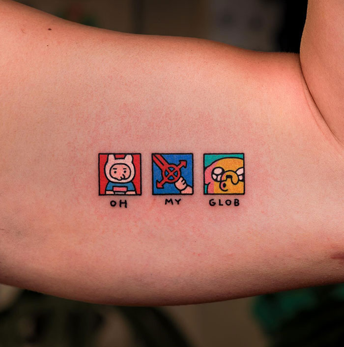 Small tattoo featuring cartoon squares with characters and text reading "Oh My Glob" on someone's skin.