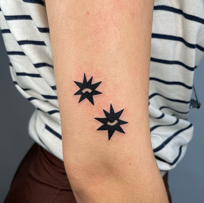 Two small star tattoos on an arm with a striped shirt, showcasing bold and minimalist tattoo ideas.