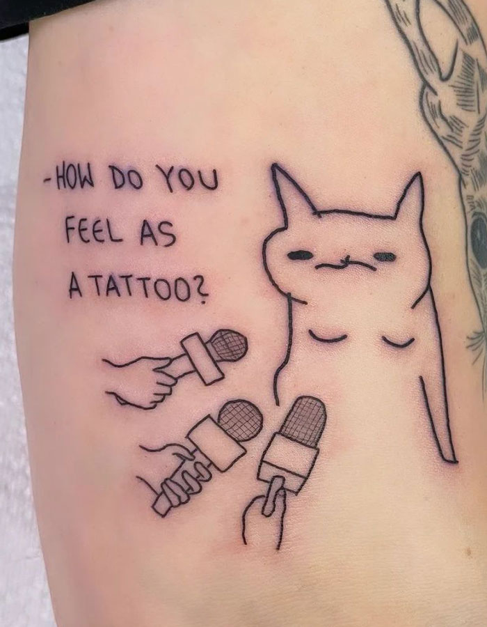 Small tattoo of a cat being interviewed, with multiple microphones and text asking about its feelings.
