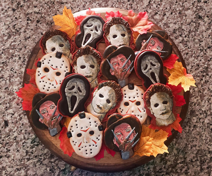 Halloween snacks featuring intricately decorated cookies inspired by classic horror movie characters on a wooden platter.