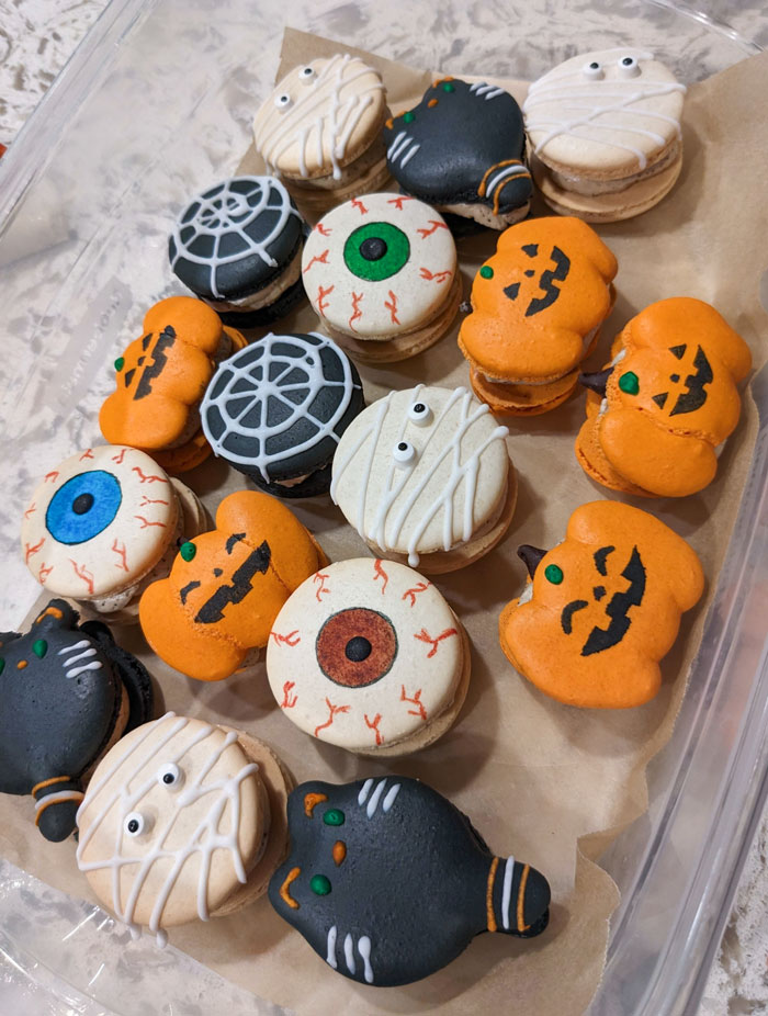 Halloween snacks with spooky eyeballs, pumpkins, mummies, spider webs, and black cat designs in a clear container.