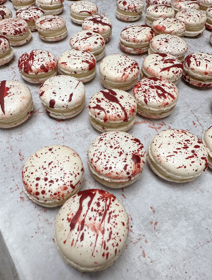 White macarons splattered with red food coloring to resemble a Halloween snack with a spooky blood-splattered effect.