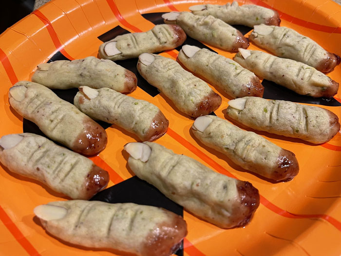 Halloween snacks shaped like creepy fingers with almond nails on a festive orange and black plate.