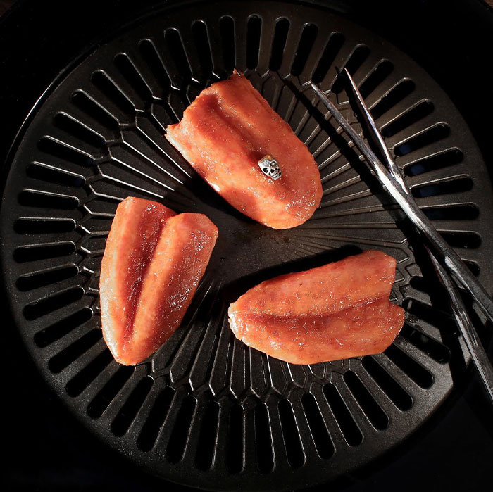 Halloween snacks shaped like realistic bloody vampire tongues arranged on a black grill plate with tongs.