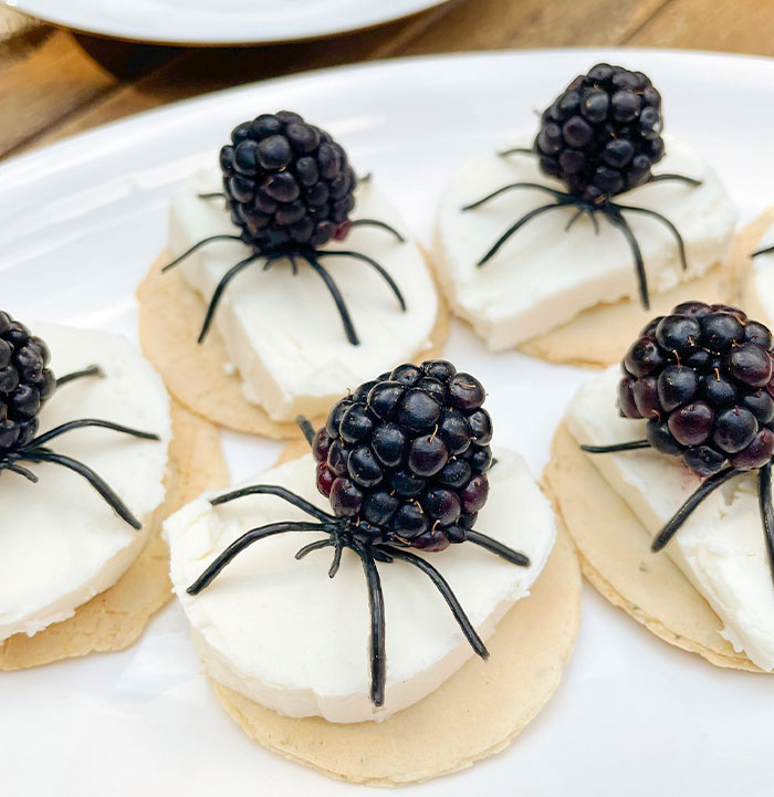 Halloween snacks with blackberries and cream cheese decorated as spiders on crackers for a festive treat.