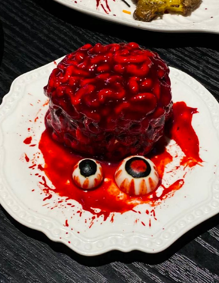 Halloween snacks shaped like a bloody brain with two edible eyeballs on a white plate, perfect for spooky treats.
