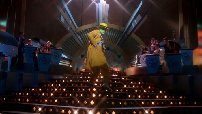 A performer in a bright yellow suit dancing on lit stairs with a live band in the background, illustrating fleeting internet trends.