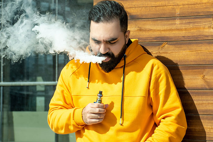 Man in yellow hoodie vaping outside, representing one of the illegal things people shared they can’t own where they live.