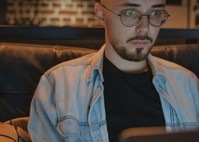 Young man with glasses focused on a laptop, illustrating people sharing normal things they can’t own due to legal restrictions.