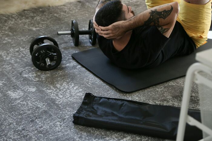 Man doing sit-ups on a mat with dumbbells nearby, illustrating people learning their hatred for fitness after trying once.