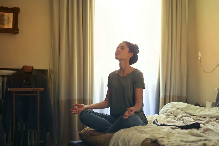 Woman sitting cross-legged on bed meditating calmly in a softly lit room, reflecting on her reaction after trying something once.