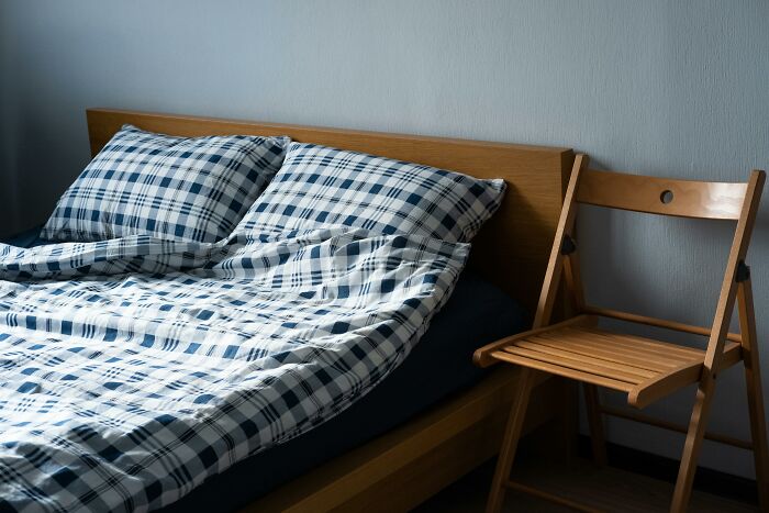 Minimalist bedroom with a wooden bed and chair, featuring blue and white plaid bedding, illustrating dislike after trying something once.