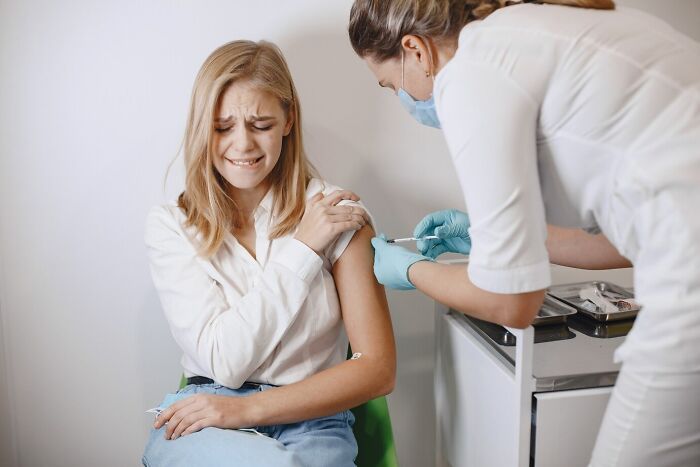 Young woman reacting nervously while nurse wearing gloves gives an injection in a clinical setting illustrating mind-blowing coincidences.