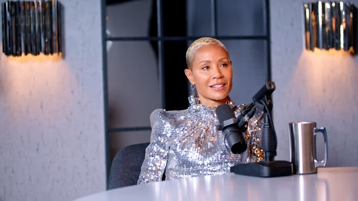 A person in a silver sequin outfit speaking into a microphone during a podcast session.