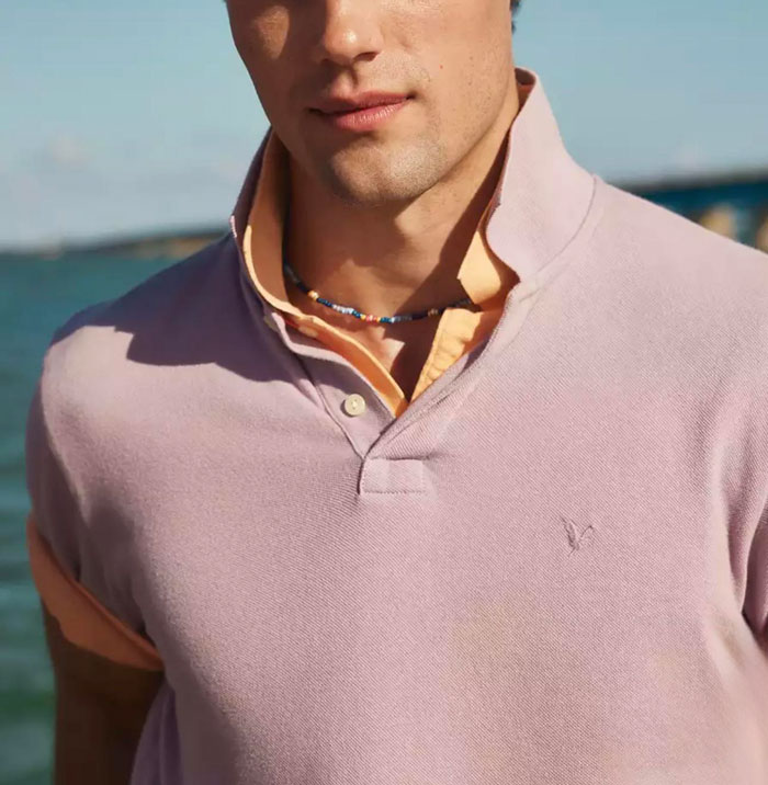 Young man wearing layered polo shirts by the water, showcasing fashion trends that disappeared quickly on the internet.