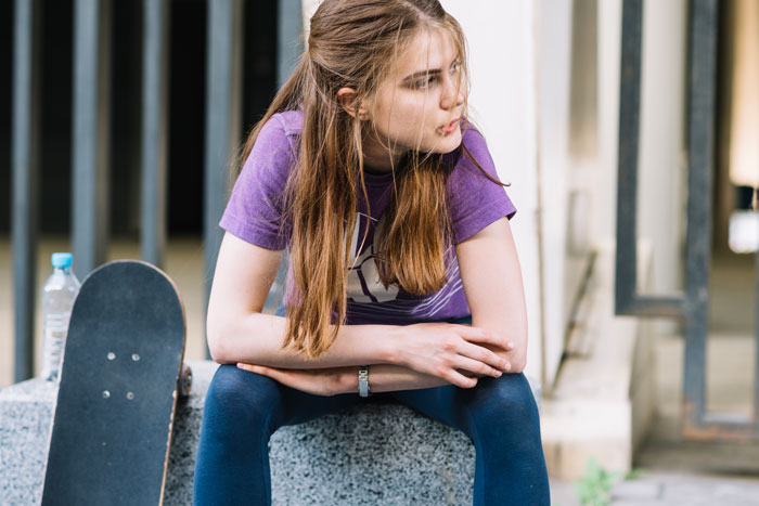Teen girl sitting on a ledge, wearing a purple shirt, near a skateboard, looking contemplative. Teen girl sitting on a ledge, wearing a purple shirt, near a skateboard, looking contemplative.