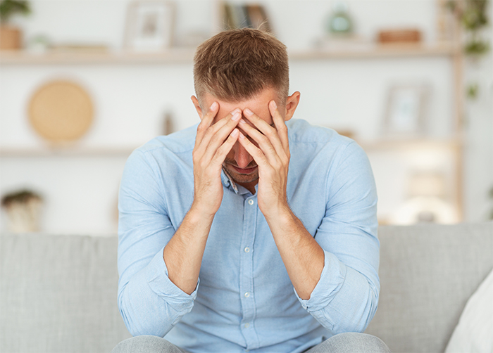 Man in blue shirt sitting on a couch, hands on head, conflicted about telling his girlfriend her filthy living habits. Man in blue shirt sitting on a couch, hands on head, conflicted about telling his girlfriend her filthy living habits.