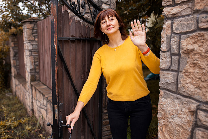 Woman in a yellow sweater waves at a stone gate, related to HOA president and new resident conflict.
