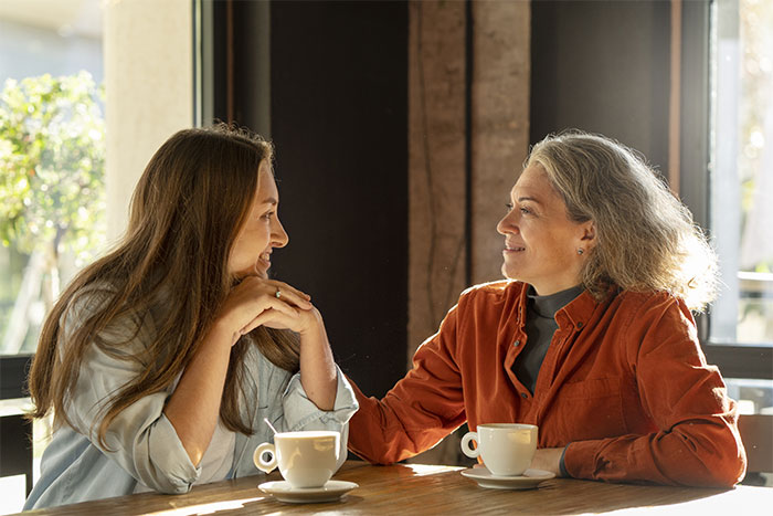 Woman and daughter-in-law sharing coffee, smiling and having a polite conversation in a cozy setting. Woman and daughter-in-law sharing coffee, smiling and having a polite conversation in a cozy setting.