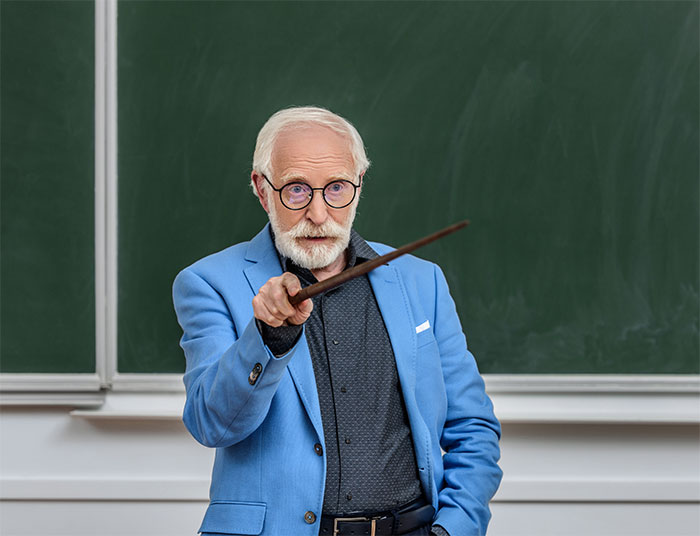 Professor in blue jacket gesturing with a pointer in front of a chalkboard.