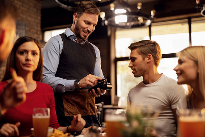 Cashier at a restaurant discreetly adds tip while processing payment for seated patrons.