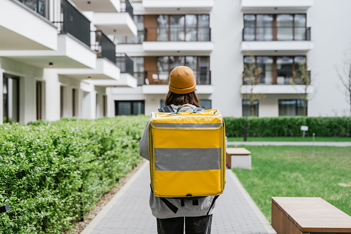 Delivery person in yellow uniform walking through a residential area.