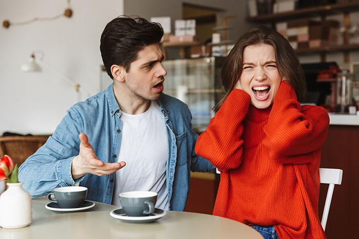 Man and woman arguing in a café, expressing emotions related to entitlement and relationship conflict. Man and woman arguing in a café, expressing emotions related to entitlement and relationship conflict.