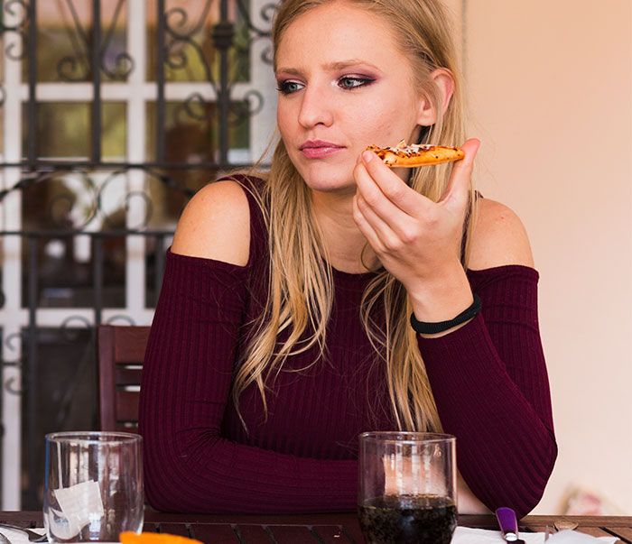 Woman holding pizza, looking displeased at dinner, symbolizes family tension over Thanksgiving invitation issue. Woman holding pizza, looking displeased at dinner, symbolizes family tension over Thanksgiving invitation issue.