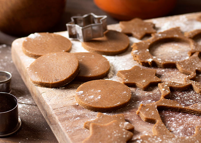 Homemade cookies being prepared on a wooden board with flour and cookie cutters. Homemade cookies being prepared on a wooden board with flour and cookie cutters.