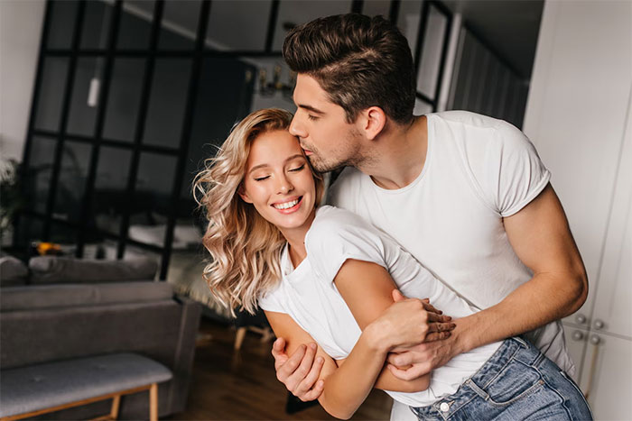 Couple embracing happily in a modern living room, symbolizing family tradition versus friendship priorities.