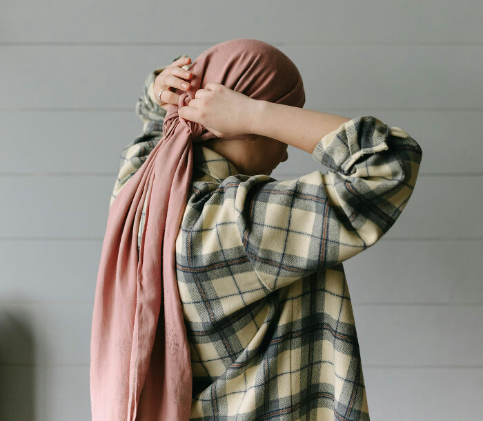 Person adjusting a pink scarf over a plaid shirt, showcasing individuality and style.