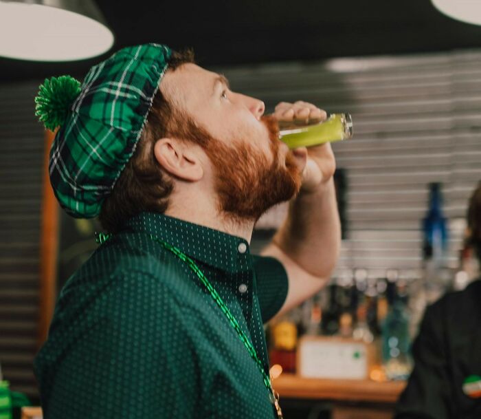 Man in green plaid hat drinking at a bar, celebrating a funny joke remembered to this day.