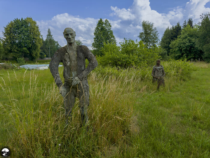 Sculptures by Adam Szubski in a grassy field, surrounded by tall trees and a blue sky.