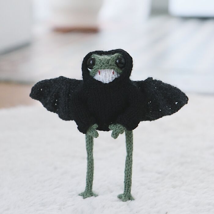 Knitted miniature frog with wings, crafted by a French knitter, standing on a soft surface.