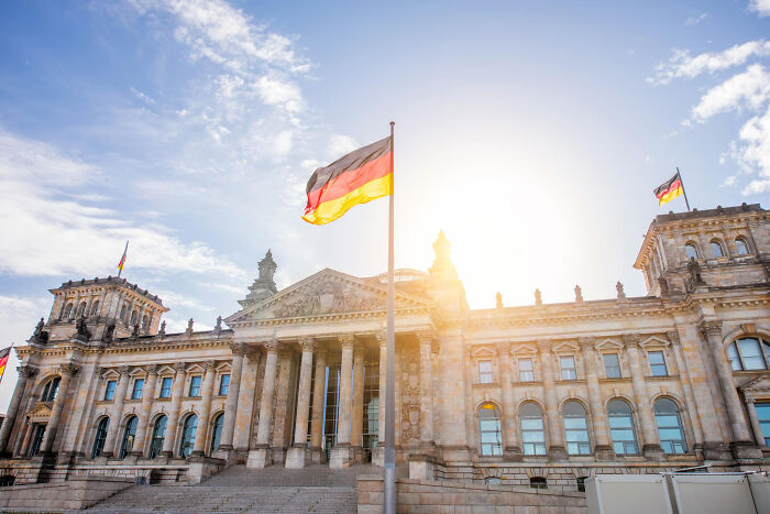 German flag waving in front of the Reichstag building under a bright sky.