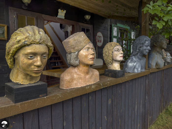 Sculptures by Adam Szubski displayed on a wooden ledge outside a rustic cabin.