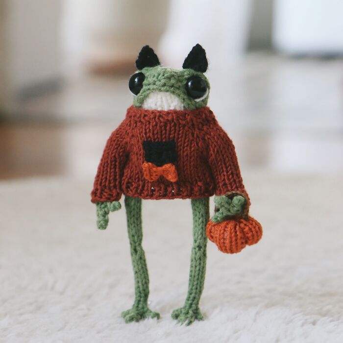 Knitted miniature frog wearing a red sweater, holding a small orange bag, made by a French knitter.