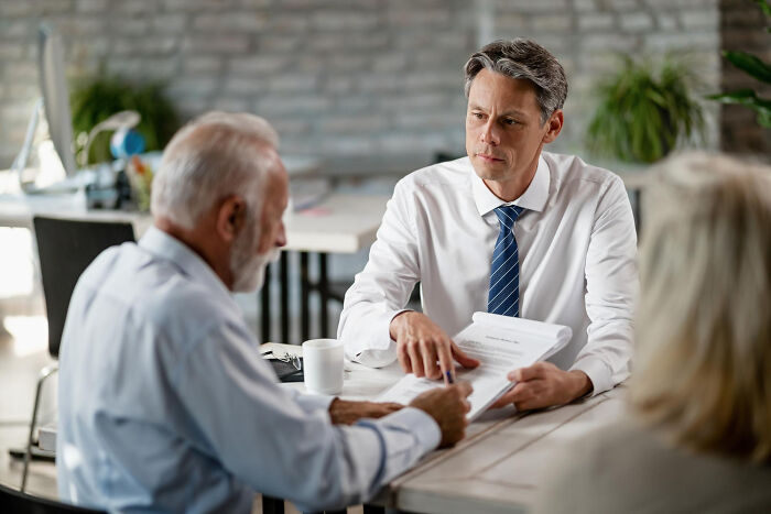 Two men in a discussion over documents, making a risky decision in a professional setting.