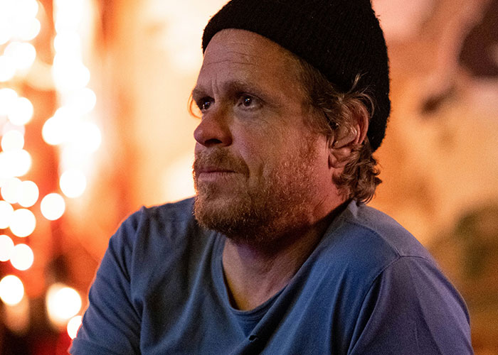Man in a blue shirt and black beanie, pondering struggles men wish women knew, with blurred lights in the background.