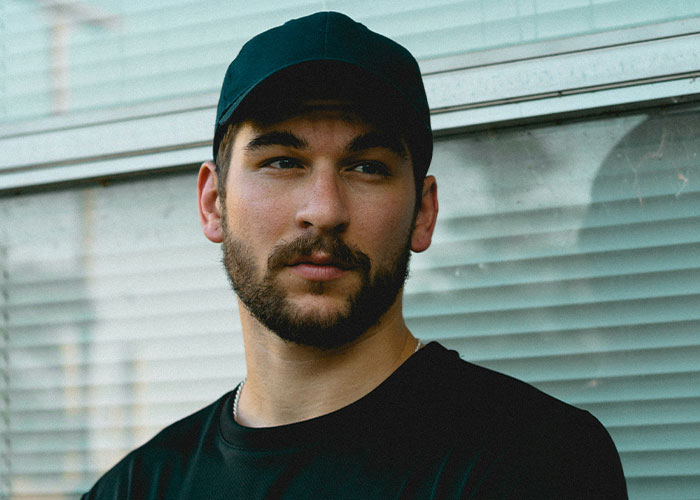Man with a beard and cap standing in front of blinds, illustrating a moment of contemplation related to savage insults.