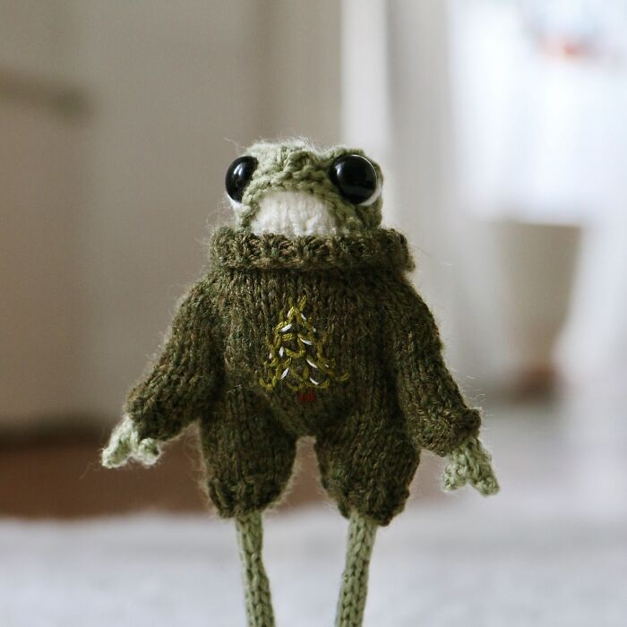 Miniature knitted frog in a green sweater with a tree design, crafted by a French knitter.